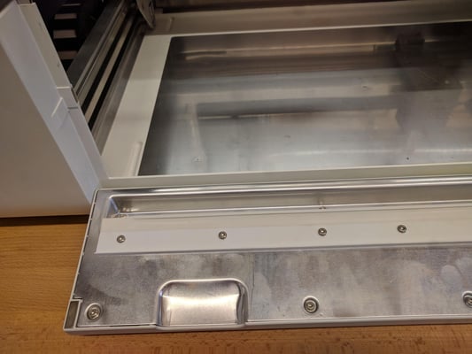 The left side of the open front door of the Glowforge. There is no debris present and the door is undamaged.