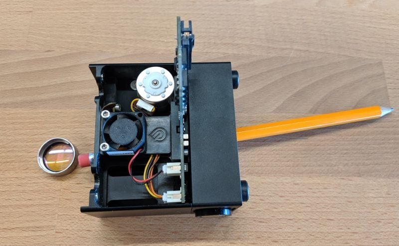 A pencil pushed, eraser side first, through the interior of the Glowforge print head. The mirror is to the left of the head having been pushed out.