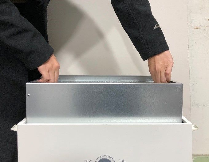 Two hands lifting a filter cartridge upwards out of the Glowforge air filter unit.