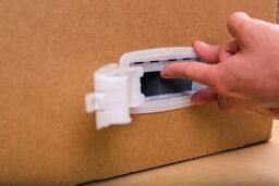 One hand holding the frame of the handle lock, the other folding the top tab towards the inside of the box