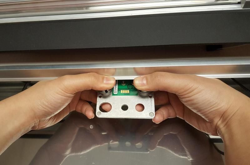 Two hands gripping the carriage plate under the Glowforge laser arm