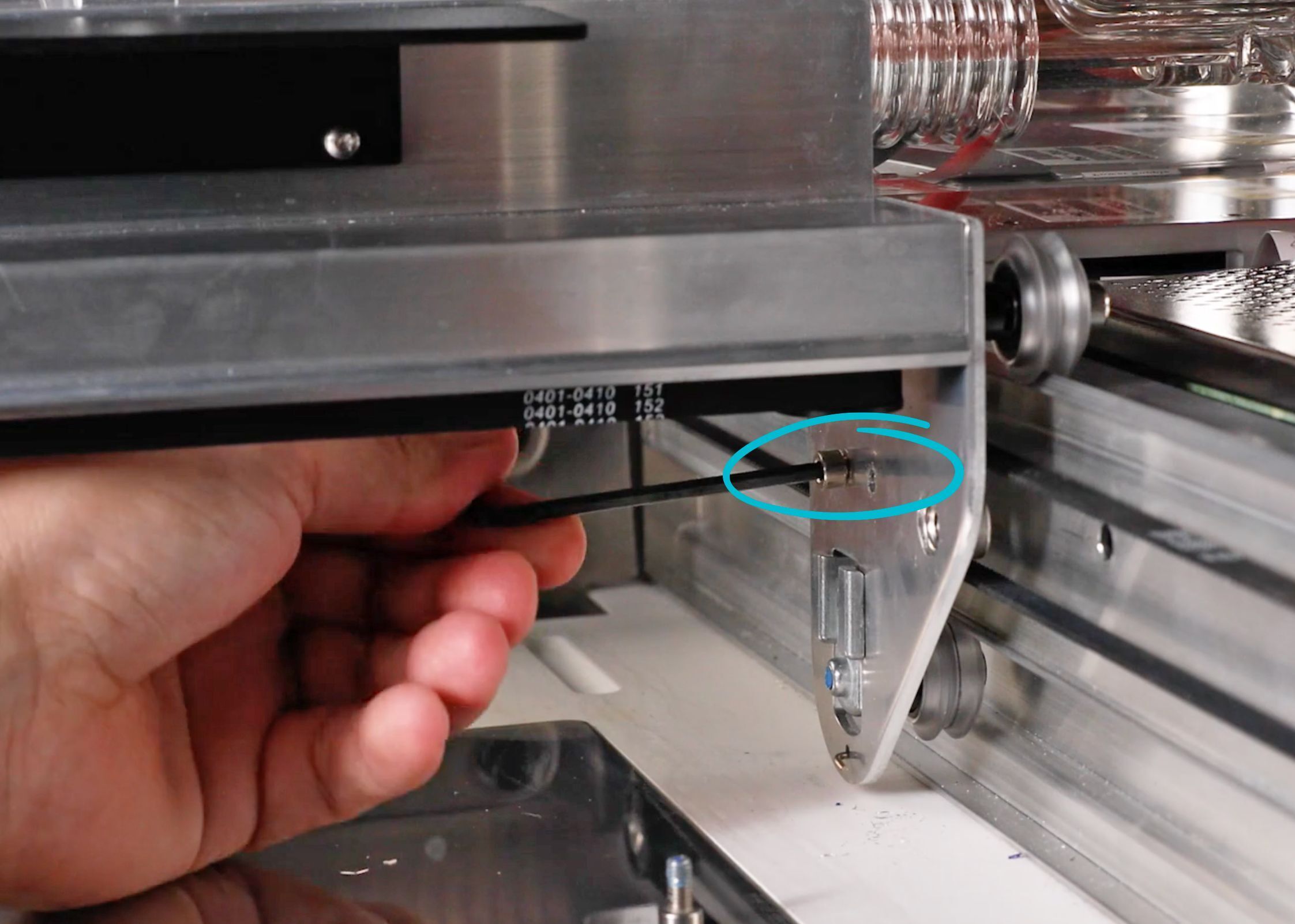 A hand using a 3mm hex key to remove the two screws below the side of the laser arm
