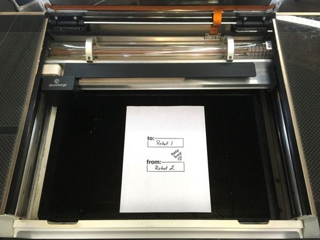 A piece of paper with hand-written lettering placed in the center of the Glowforge print bed