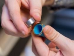 One hand grasping the Glowforge lens tool, the other lifting the lens off the tool