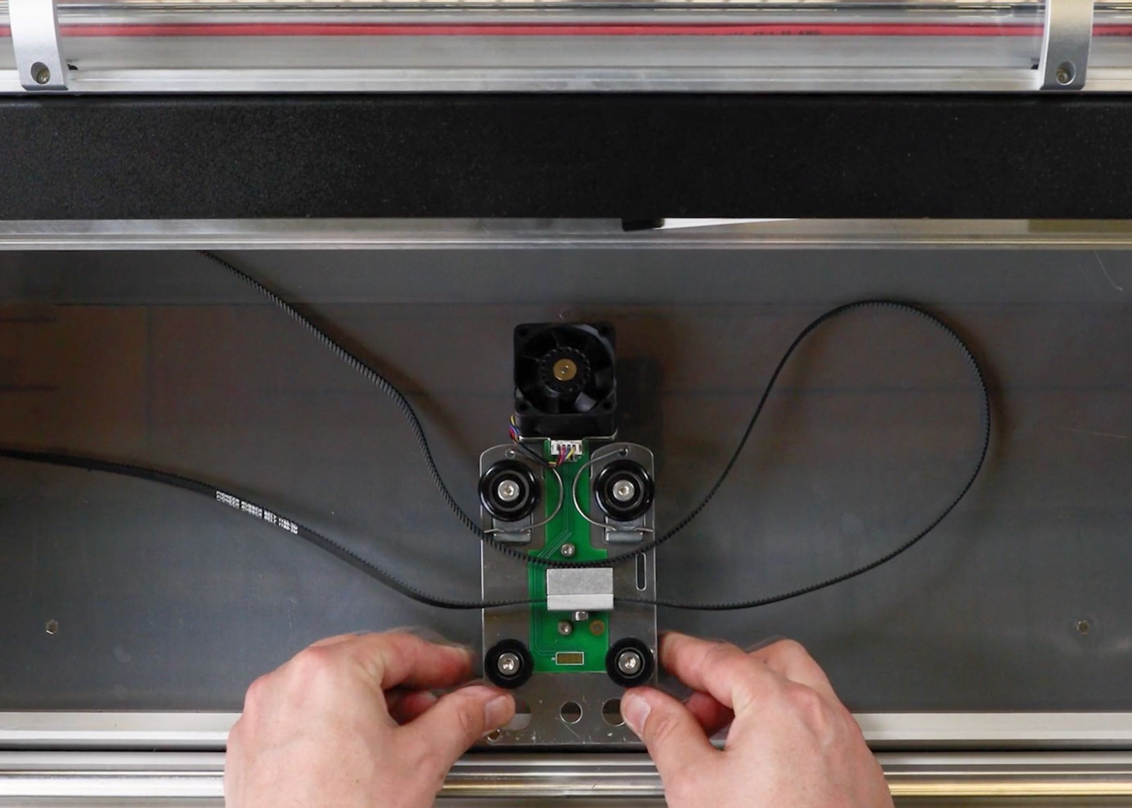 The carriage plate resting on the bed of the Glowforge with it's belts laid out without twists or overlaps