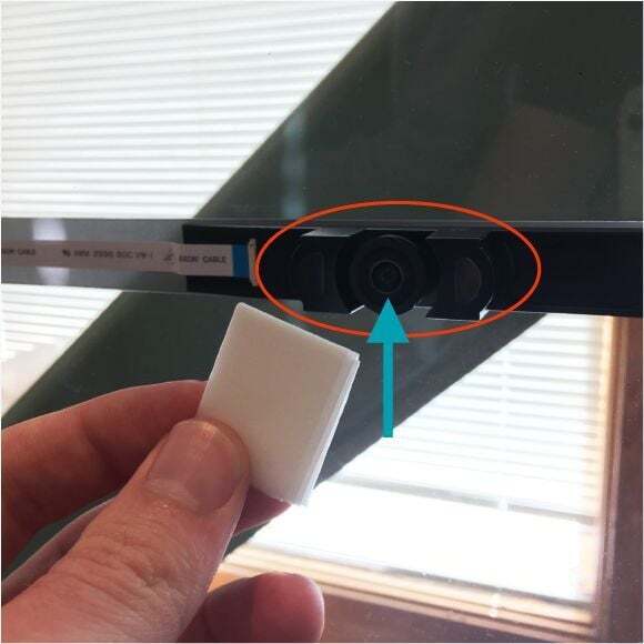 A hand holding a lens wipe and cleaning the lens of the Glowforge lid camera