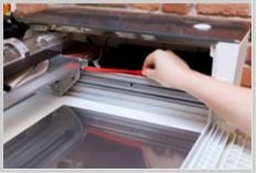 Hand removing red, silicone strip from the side rail of a Glowforge printer's interior