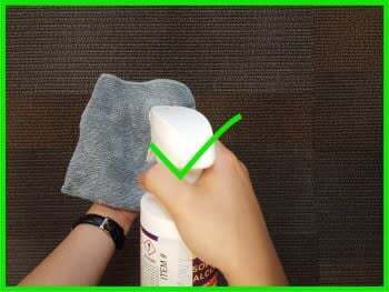 One hand holding a lint-free cloth, the other spraying isopropyl alocohol onto it