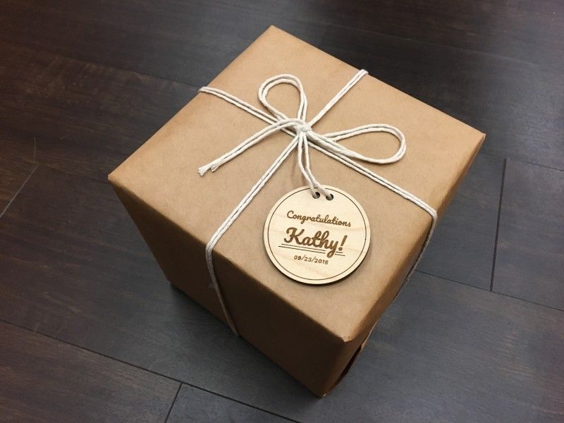 A package wrapped in brown paper and string with a custom, laser cut and engraved wooden tag