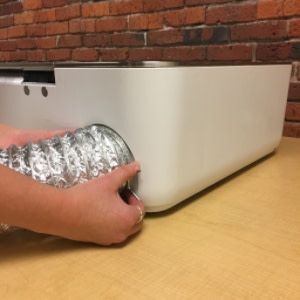 Two hands attaching using a ring clamp to attach the exhaust hose to the back of the Glowforge