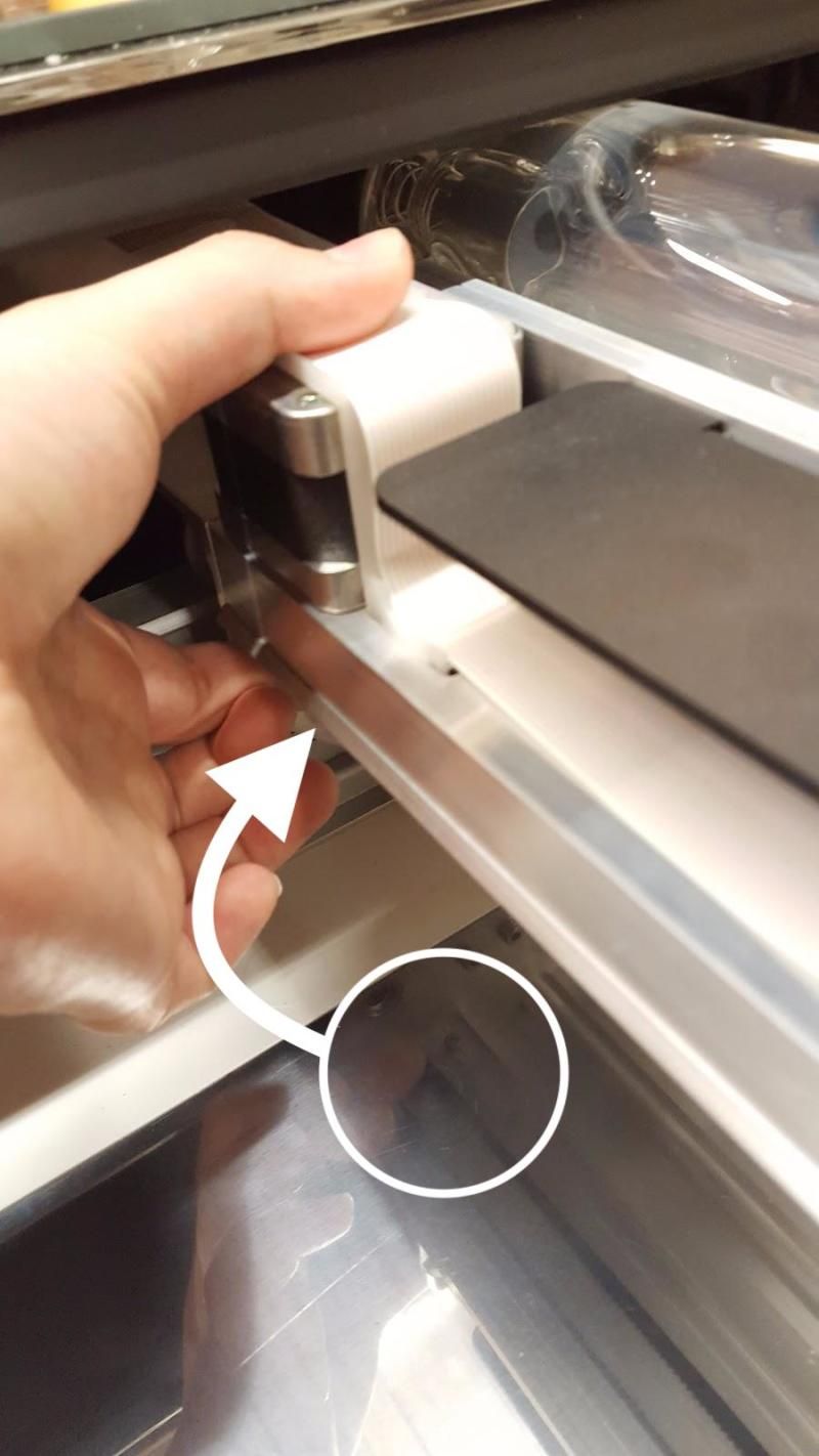 A hand grasping the laser arm and using pressure to hold the belt to the pulley on the underside of the laser arm