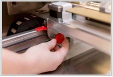 Hand unscrewing a knob from the side of the laser arm in a Glowforge