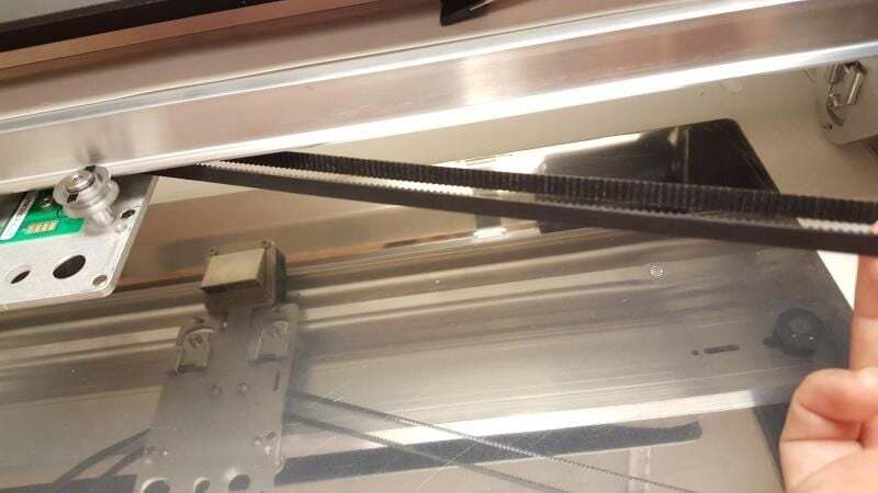 A hand stretching the belt towards the right side of the laser arm